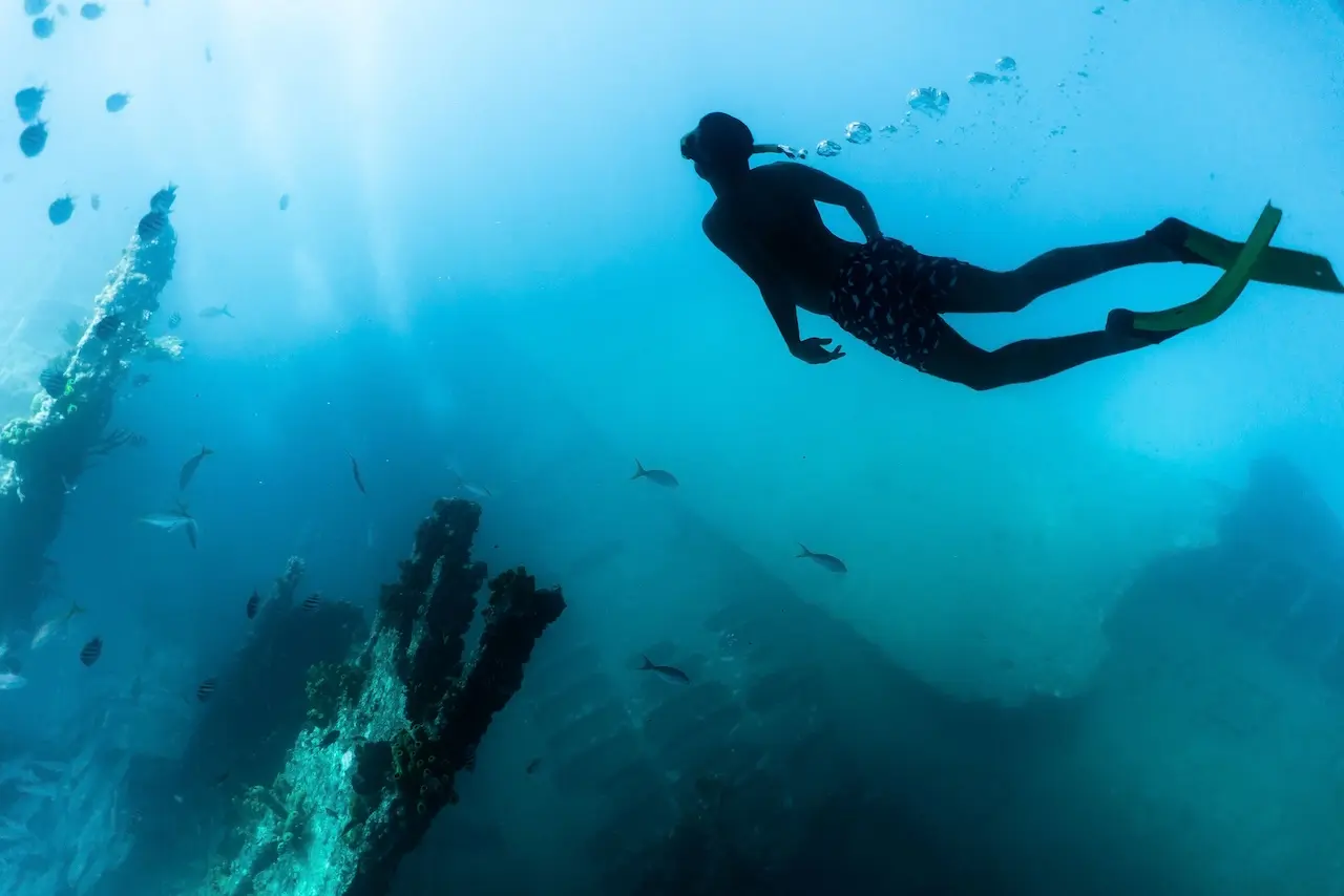 A Red Sail Aruba scuba diver silhouetted underwater against blue water.