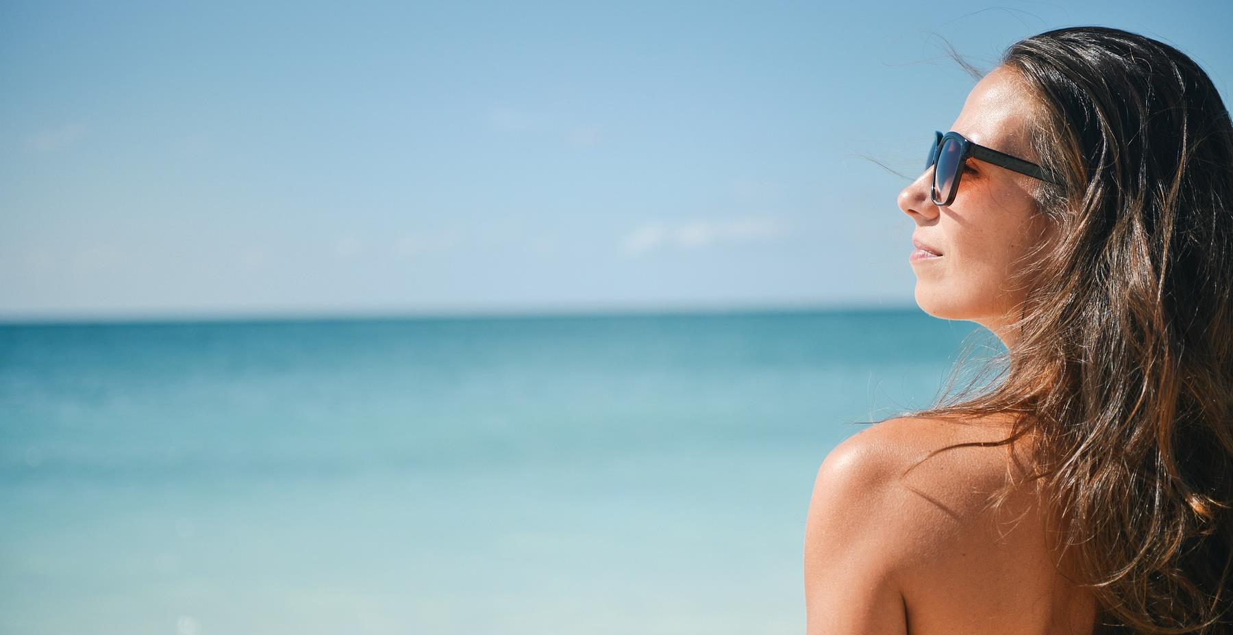 A girl wearing sunglasses looking out at the sea.